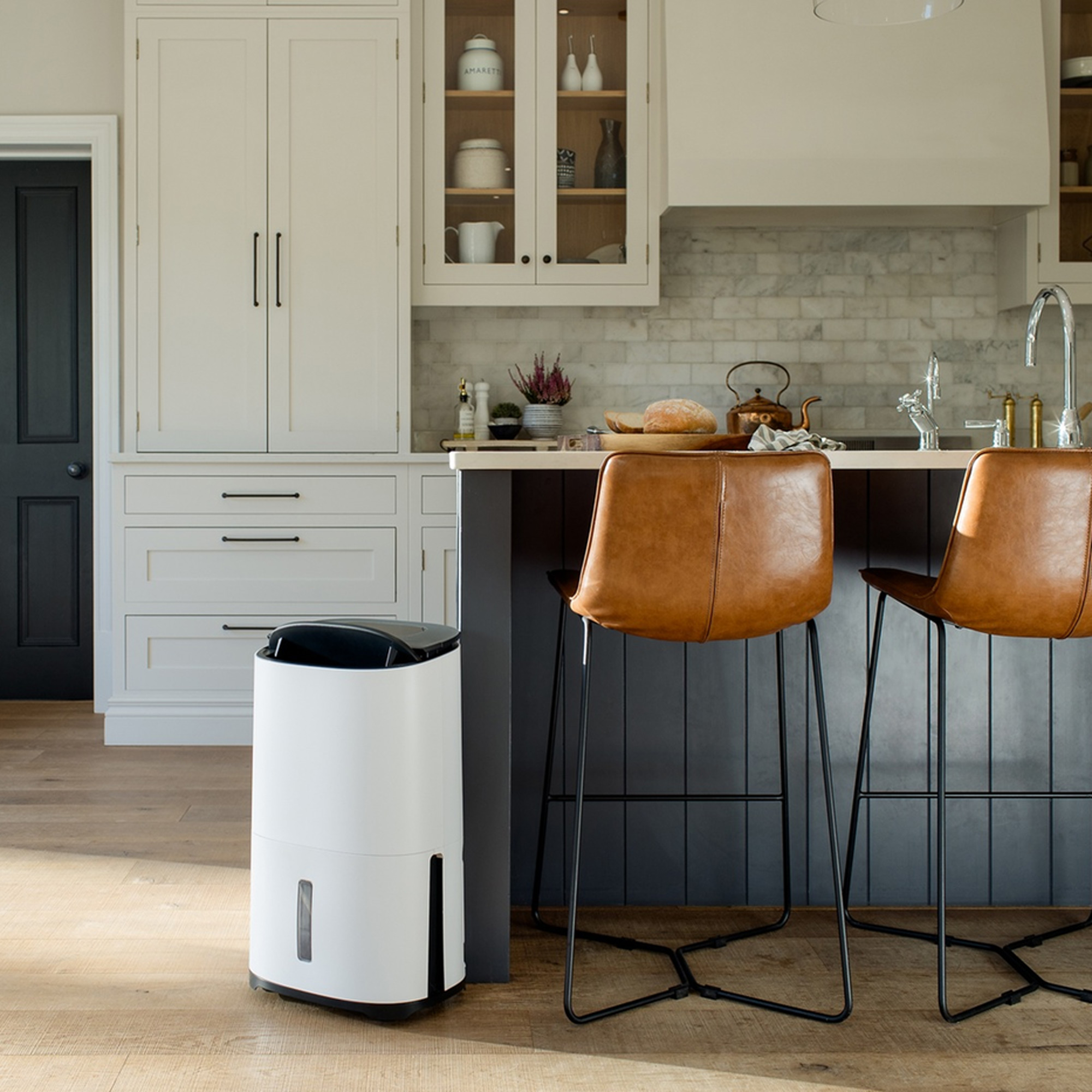 a black and white shaker kitchen with a Meaco dehumidifier beside a kitchen island with leather upholstered bar stools