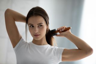 Young woman brushing hair in bathroom before washing