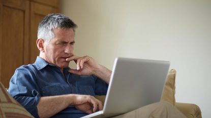 Perplexed older man using laptop on sofa