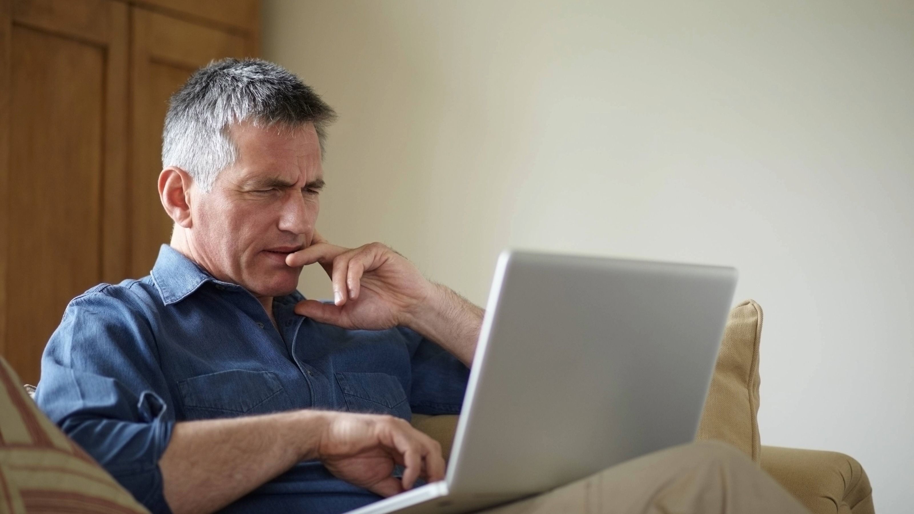 Perplexed older man using laptop on sofa