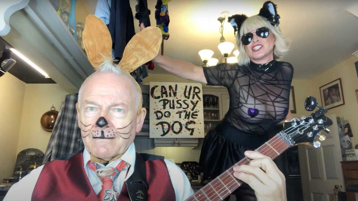 Toyah and Robert Fripp in their kitchen. Robert is wearing face paint to make him look like a cat, while Toyah is dancing on the table