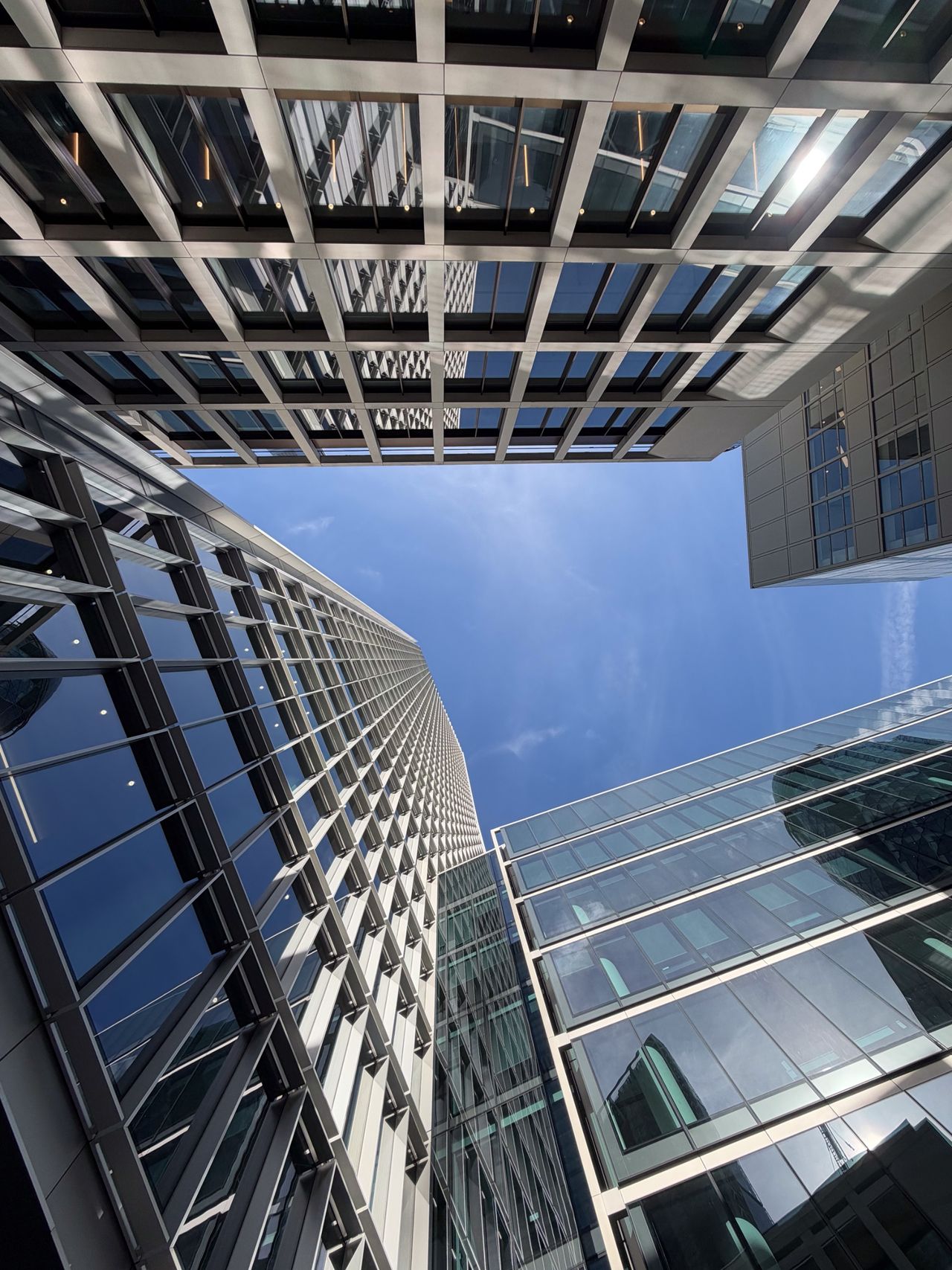 Upward view between modern glass-and-steel office buildings framing a clear blue sky.