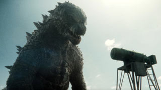 Godzilla standing next to a tiny object