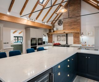 large T shaped kitchen island with blue cabinets, white worktops and blue stools running along one side