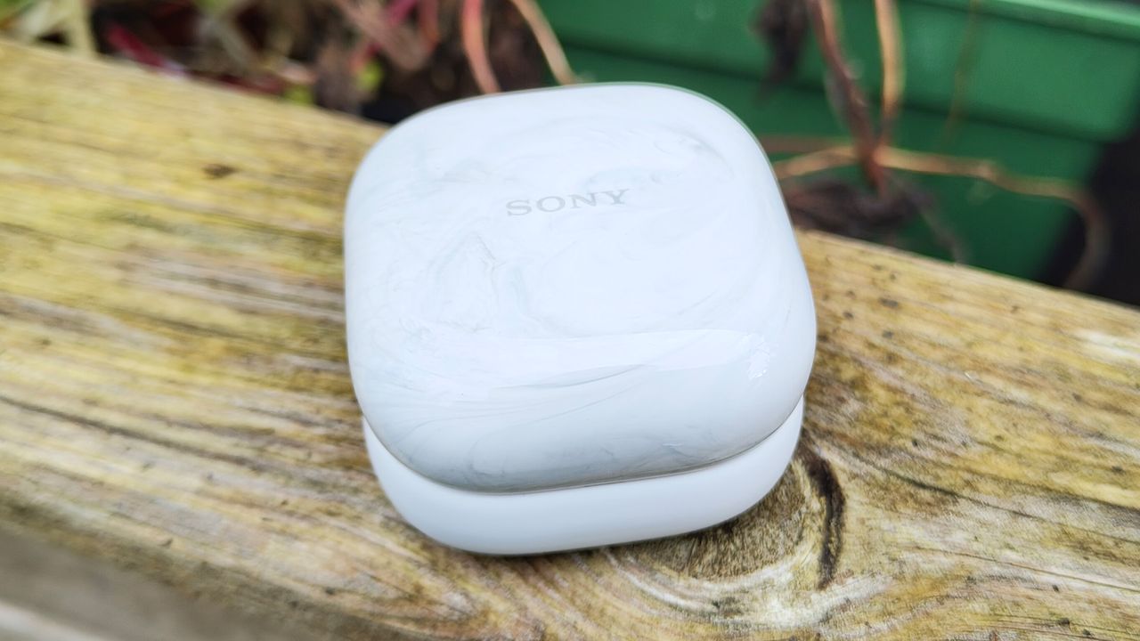 The white charging case for a pair of Sony LinkBuds Fit in-ear headphones, sitting on a wooden bench.