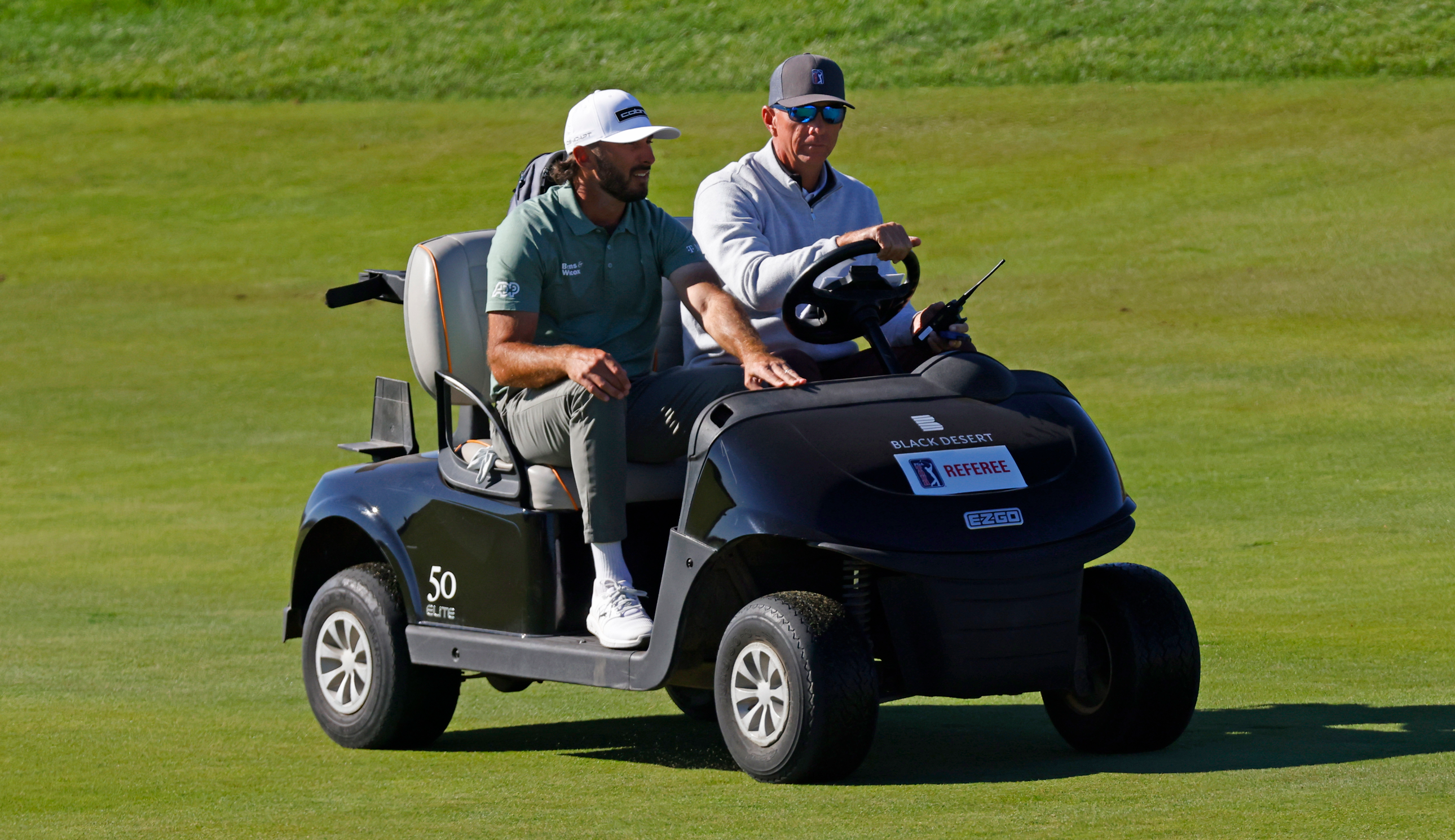 Max Homa rides a golf cart with a referee 