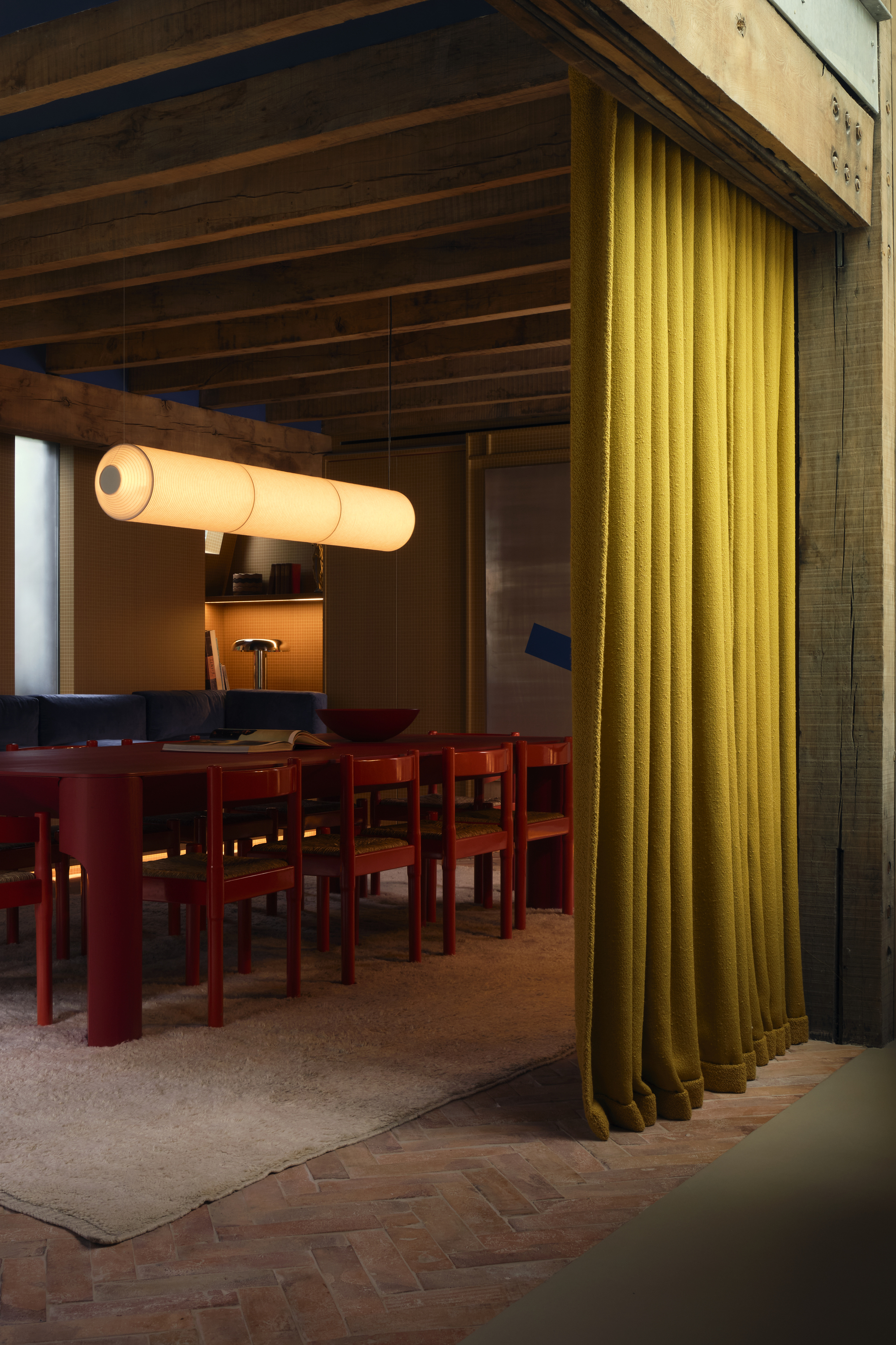 Image of a moody dining room iwth a red table and chairs and a pendant light hanging overhead. There is an ochre yellow curtain in the doorway.
