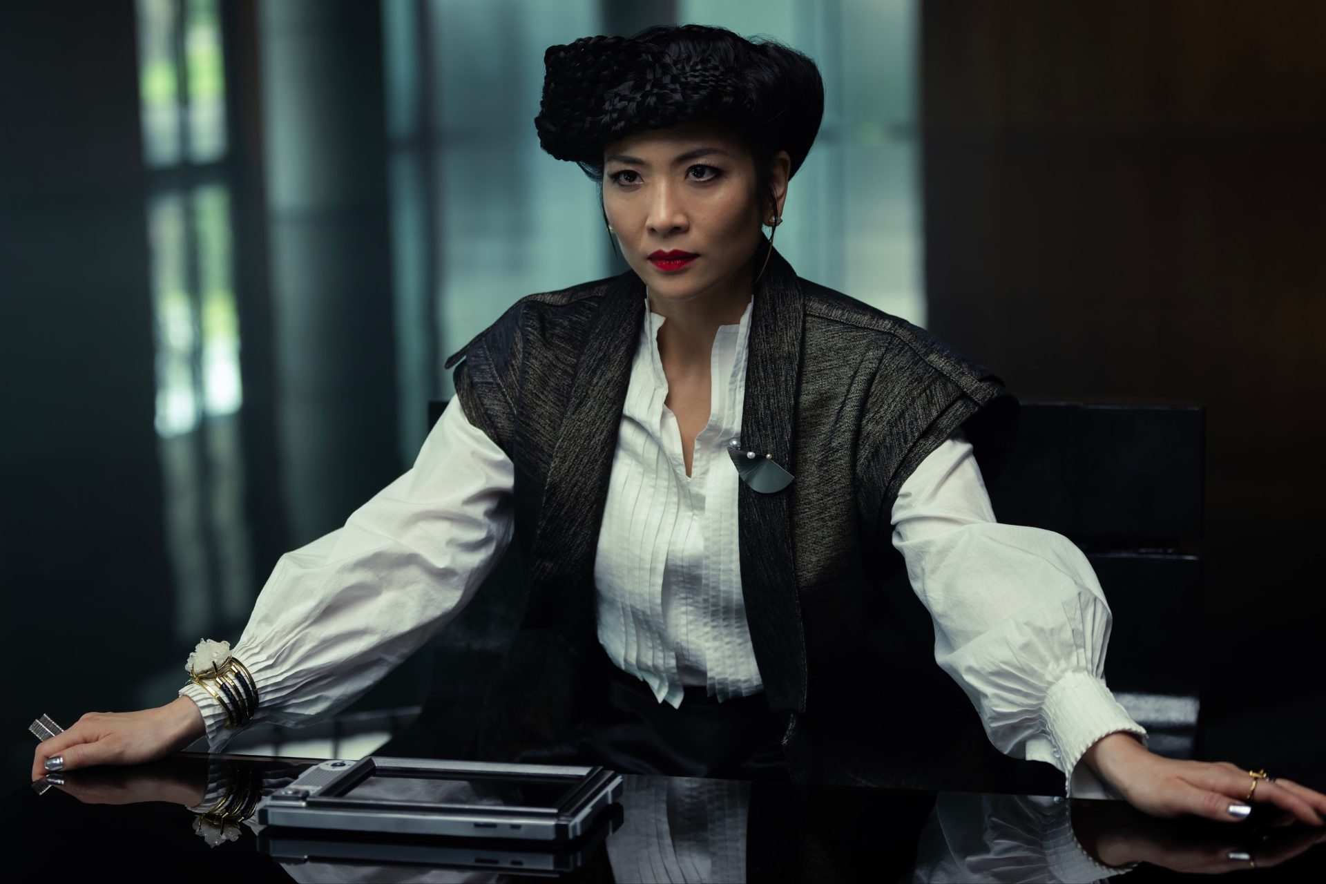  Earth. A well-dressed woman has her hands on a desk in front of her. She has a stern look on her face.