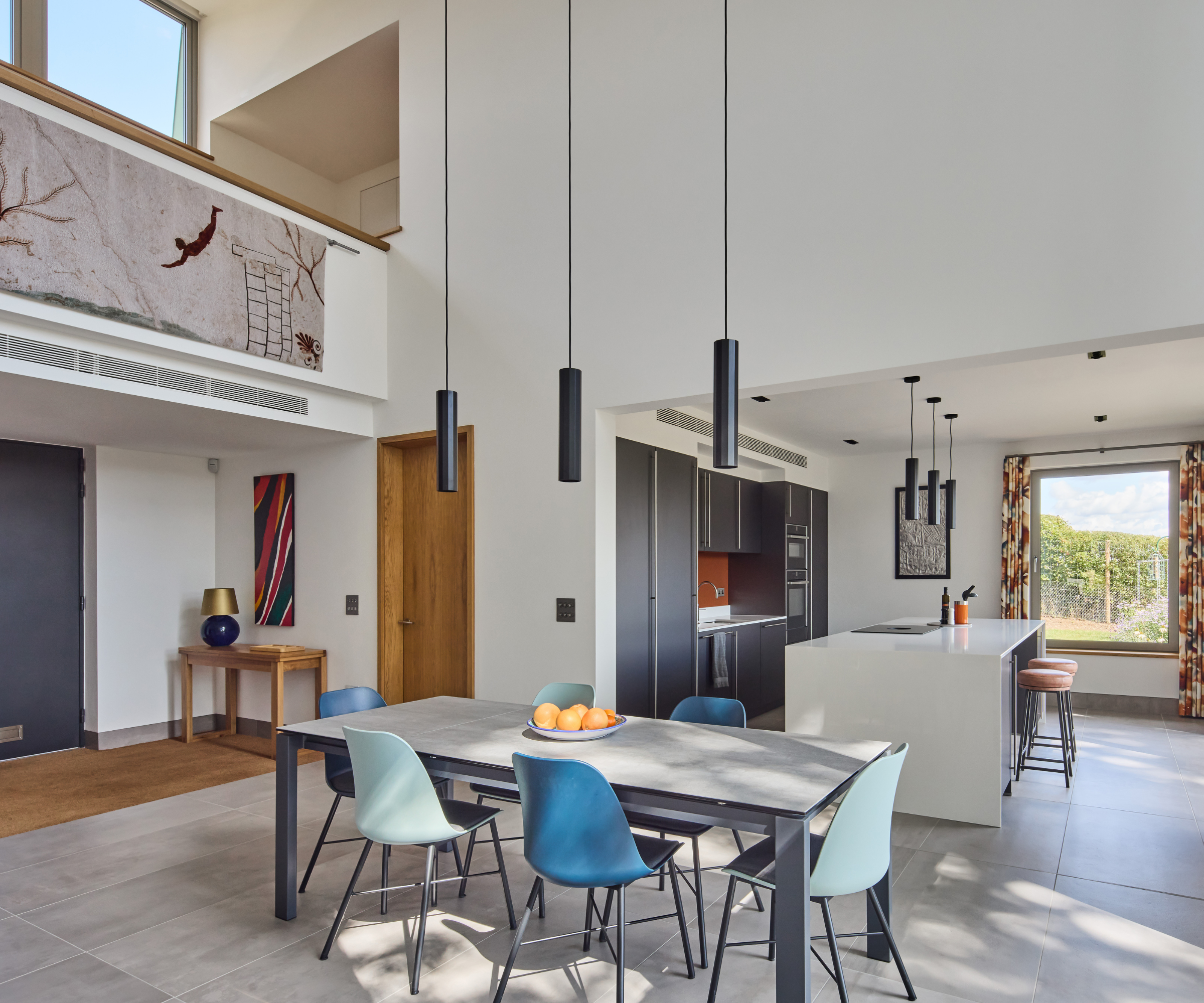 Open plan diner and kitchen with pendant lights over the dining room table and a kitchen island in the background
