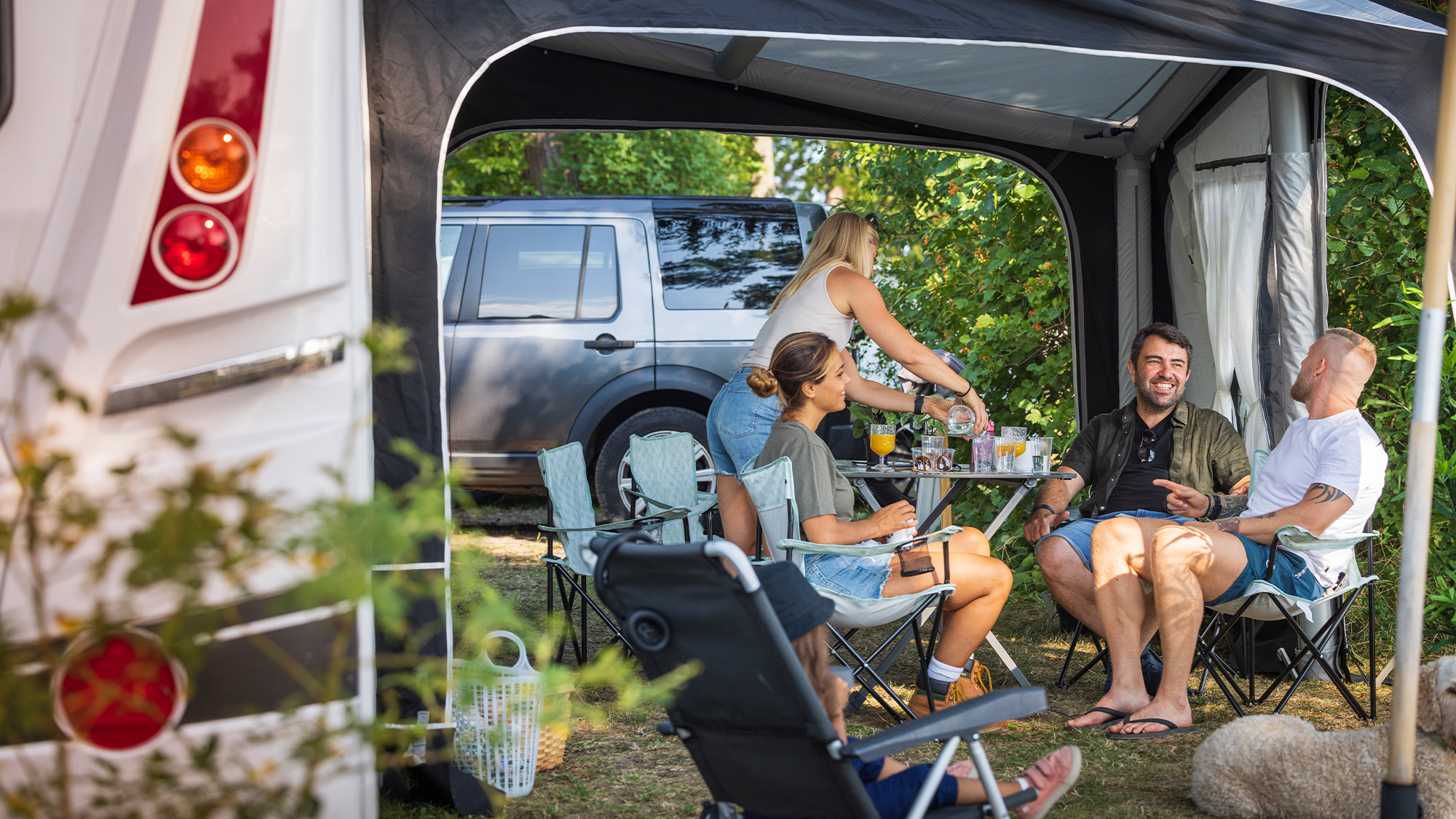 Four adults sitting outside a caravan on a campsite