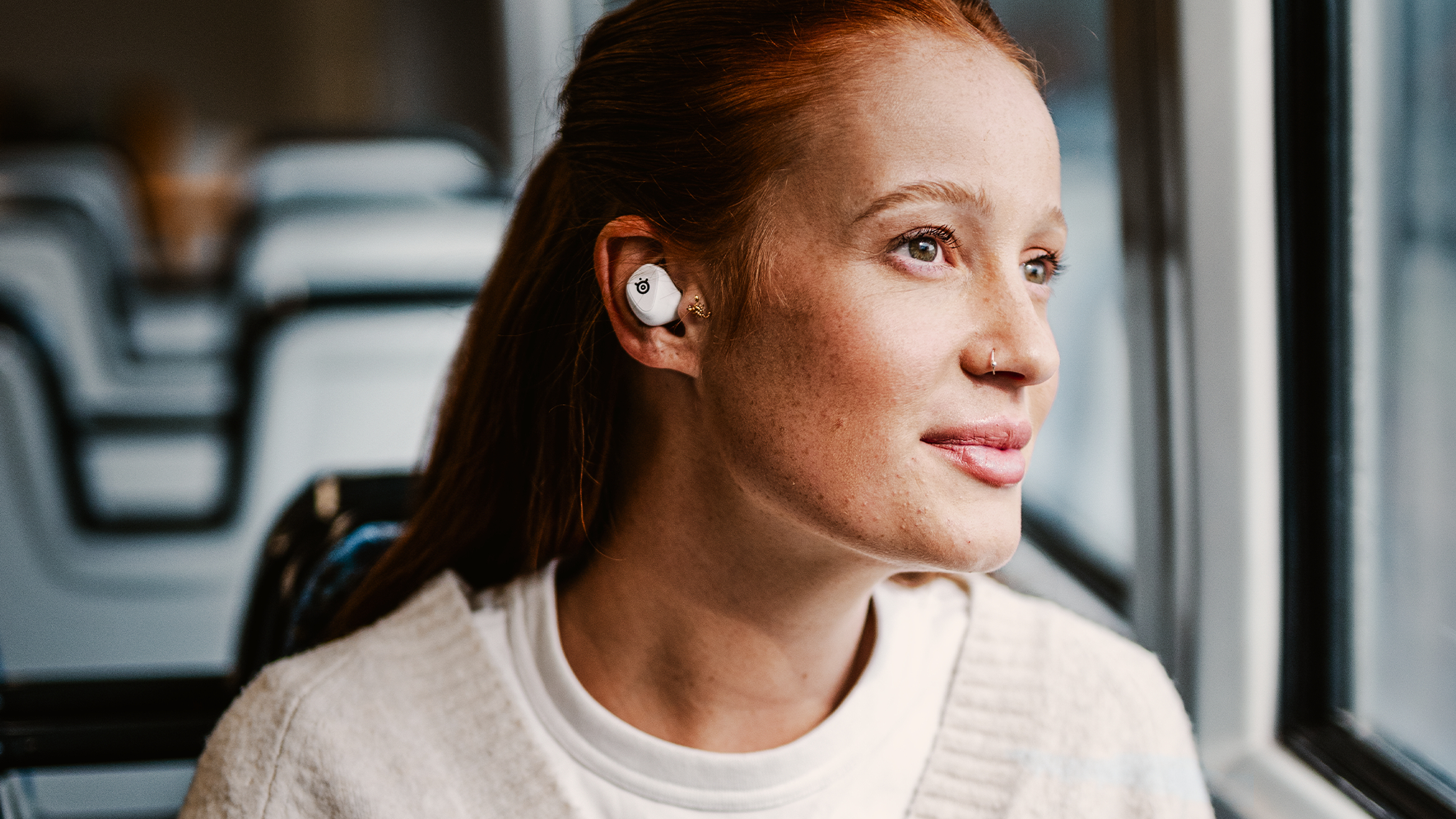 The SteelSeries Arctis GameBuds being worn by a female on public transport