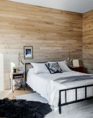 Rustic bedroom with wood panelled walls and black iron bed