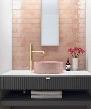 Tiled pink bathroom, with pink basin, gold tap and white counter top. a gold rimmed mirror hanging on the wall