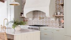 Neutral kitchen with light sage green cabinets, tiled wall, marble countertop