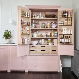 Neptune larder in dusty pink with doors open and shelves filled with kitchen items next to complementary cupboard units in a kitchen