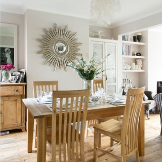 Neutral dining room with wooden table and chairs and sunburst mirror on wall