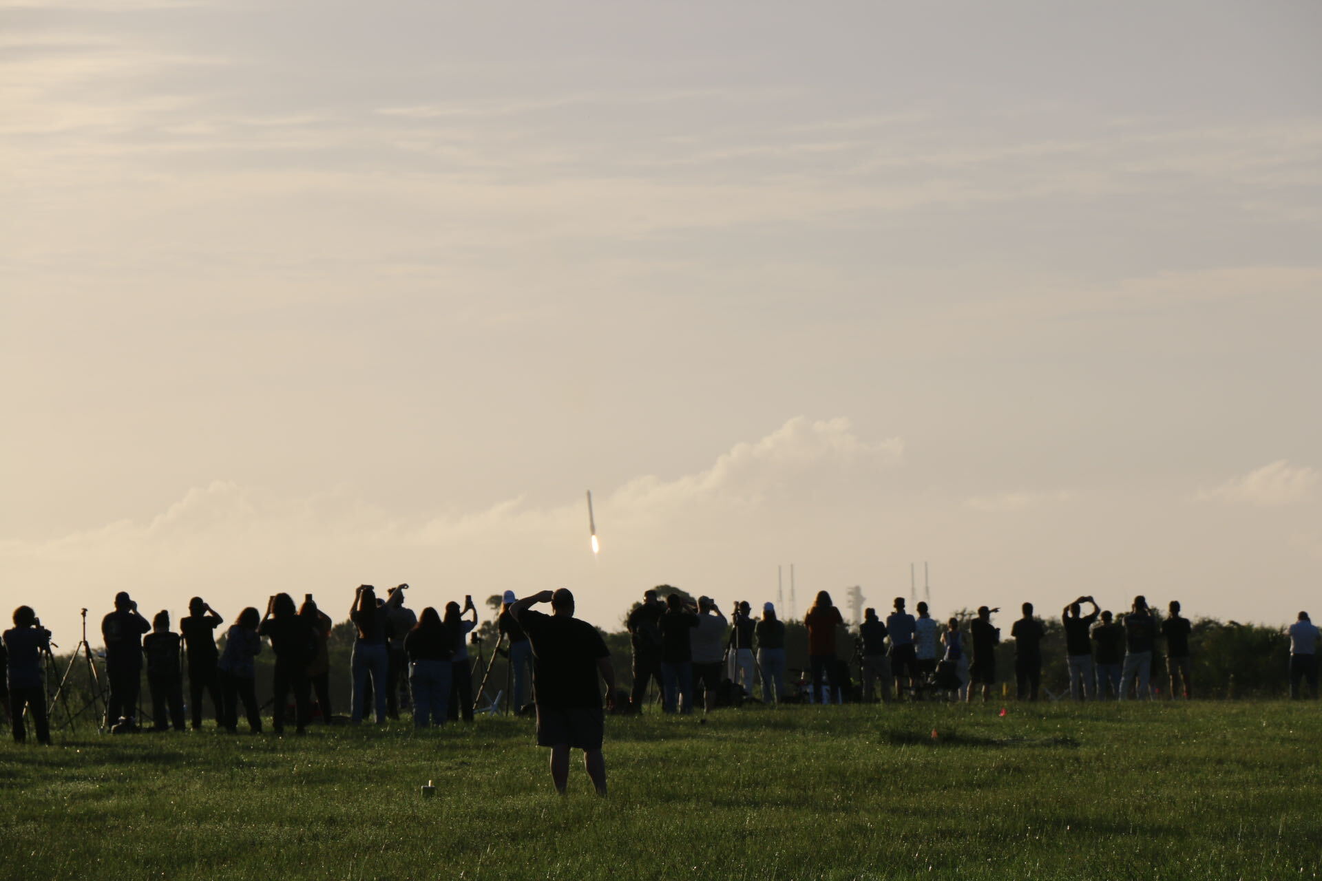 People stand on a lawn watching a long structure descend to Earth.