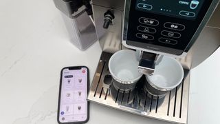 Looking down onto the De’Longhi Dinamica Plus as its ready to paur an espresso with the app onpen on a smartphone to the left-hand side