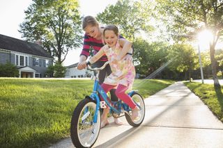 parent teaching little girl how to ride a bike