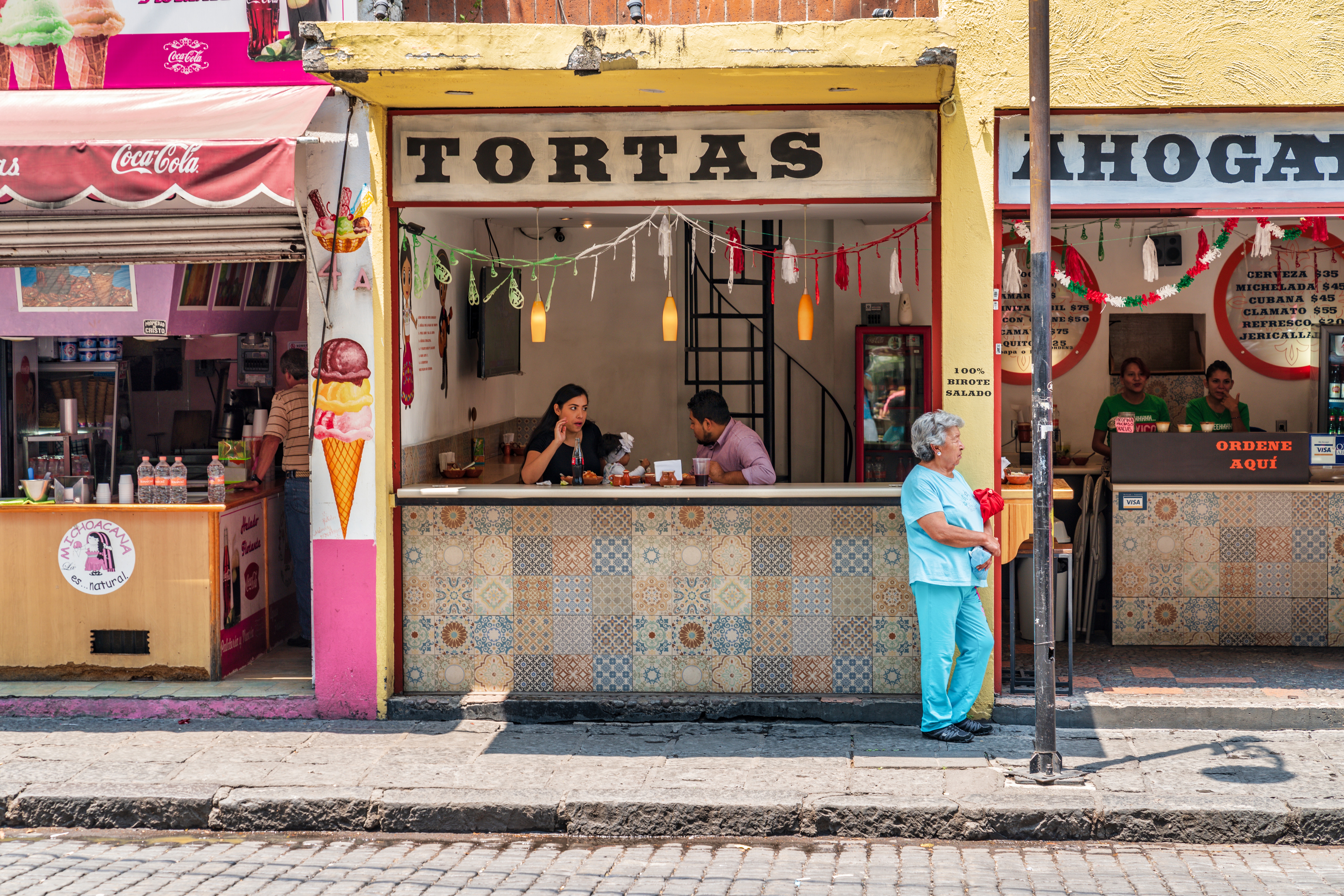 A series of sun-lit street photography shots of Mexico City portray a vibrant destination characterized by contrasting architectural styles, tropical plants, and bright colors.