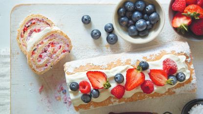 Low-fat gluten-free roulade on a wooden board with two slices cut and bowls of fresh fruit to the side