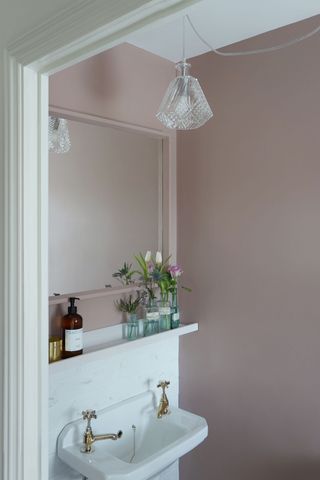 a pale pink bathroom with a white sink, a mirror and a shelf