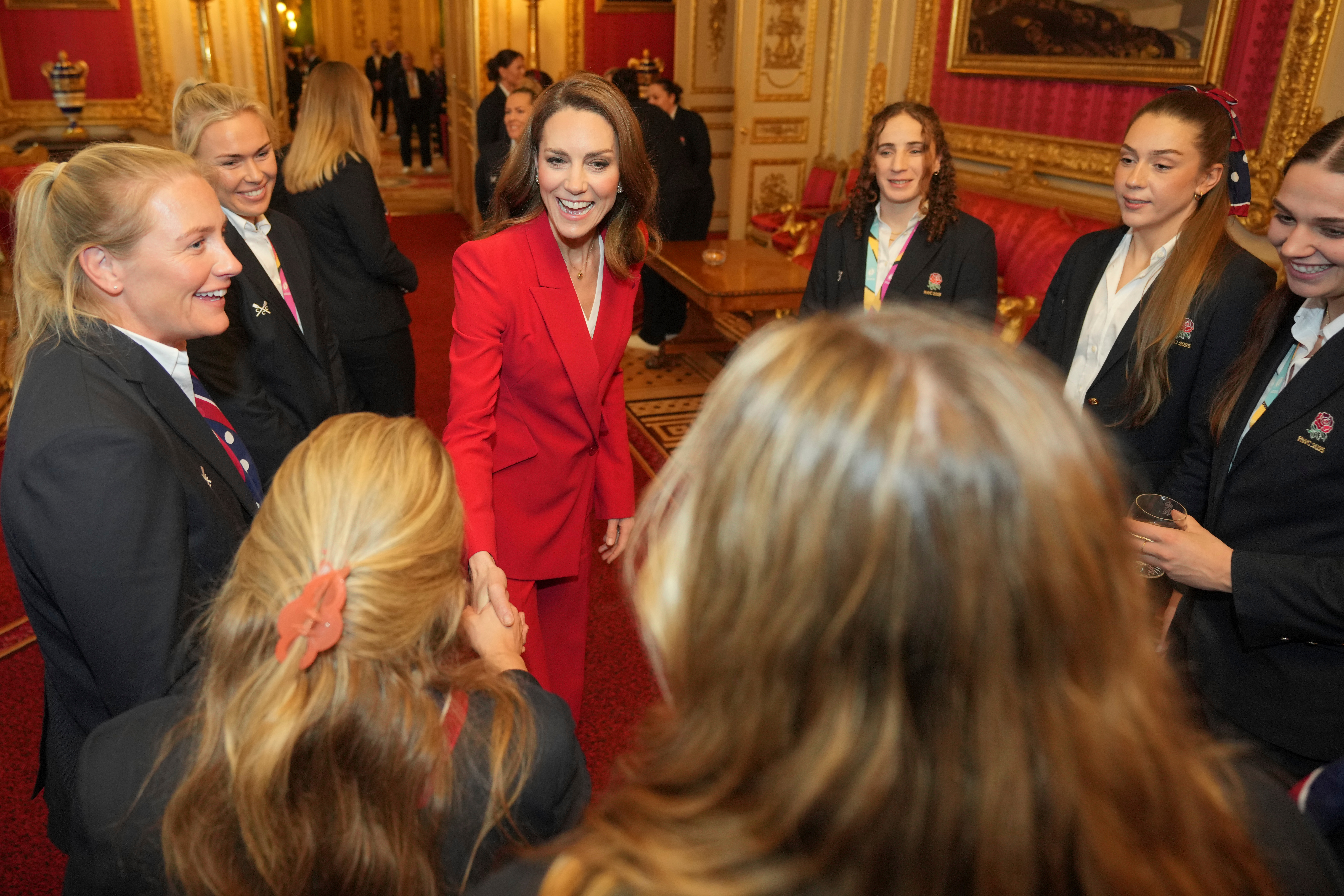 Princess Kate wearing a red suit shaking hands with members of the England women's rugby team