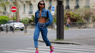 Emilie Joseph wears black large sunglasses, small crystal earrings, a navy blue denim cropped cargo jacket, a matching navy blue denim with embroidered rhinestones / crystals striped pattern V-neck / cropped bra tank-top, navy blue denim double waist large pants, neon pink shiny satin pointed pumps heels shoes , during a street style fashion photo session, on April 30, 2023 in Paris, France.