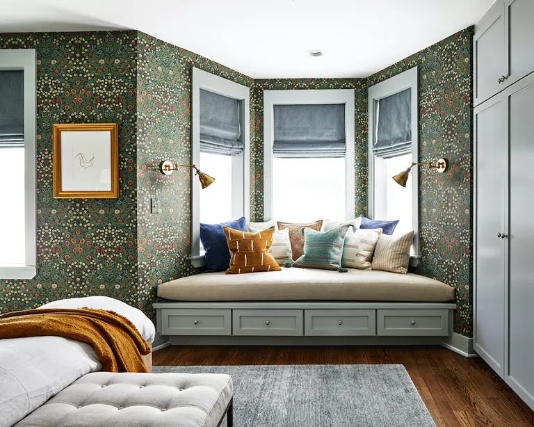 A bedroom with green floral wallpaper and a built-in storage seat in the bay window