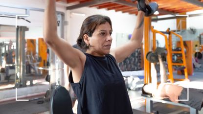 Woman lifting dumbbells above her head in a shoulder press at the gym with equipment surrounding her, representing how often should you lift weights