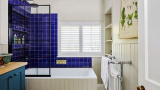 bathroom with shower over bath and blue tiles and window shutters
