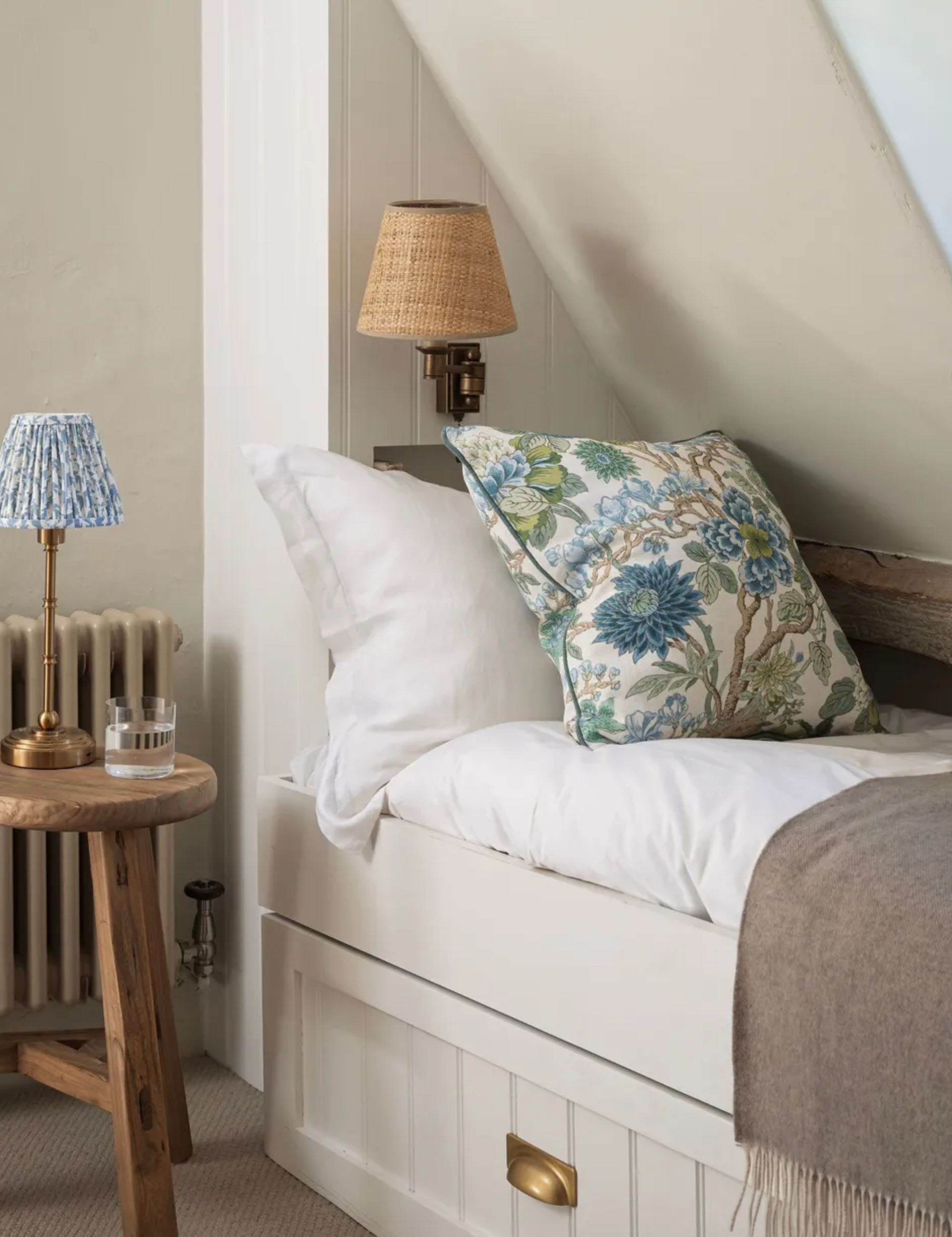 neutral loft bedroom with a trundle bed built into the sloped ceiling with a pull out base, styled with blue and green floral cushion with an antique side table as the nightstand