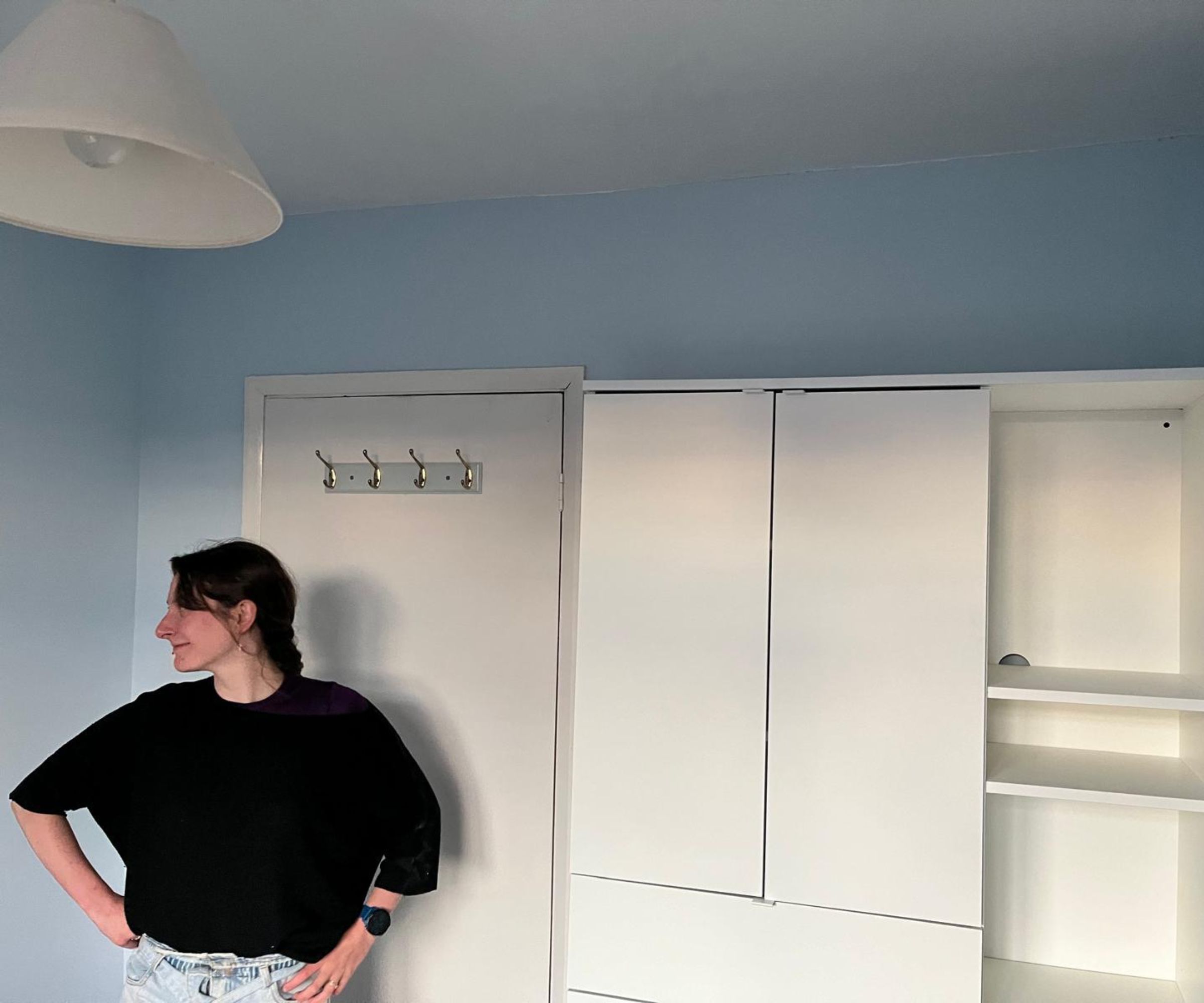 A woman in a black top stands proudly beside a newly fitted white wardrobe and shelving unit in a pale blue painted room.