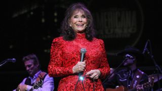 Loretta Lynn smiling on stage in a bright red dress.