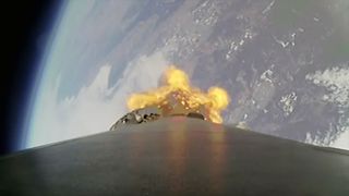 a camera mounted on the side of a rocket captures a downward looking view showing the booster, its fiery engine plume and the Earth below