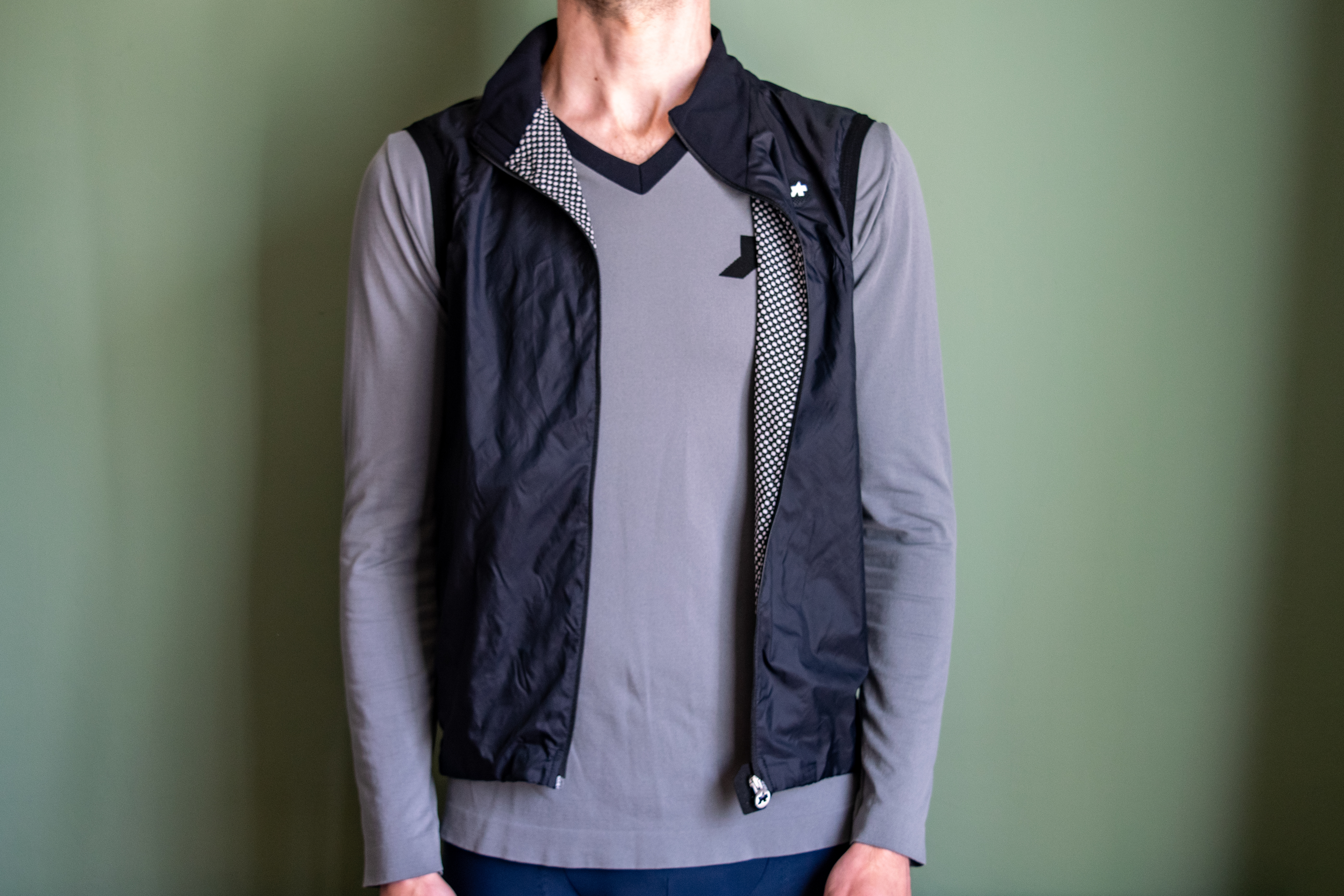 A man wearing a black Assos Tactica gilet over a grey long sleeve shirt