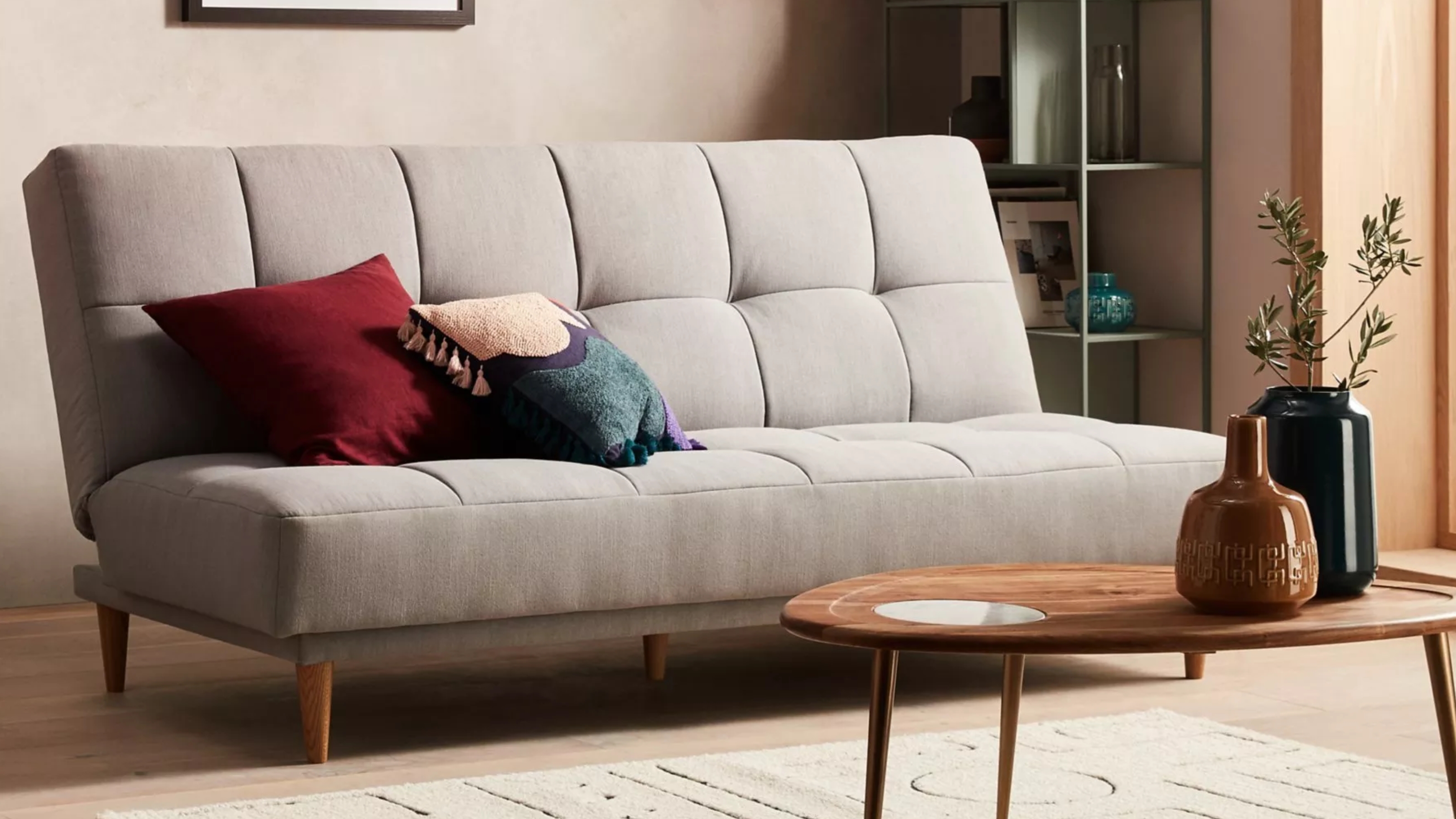 a modern grey sofa bed in a neutral room with a wood coffee table and vases