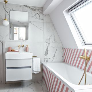 A feminine pink and white bathroom with marble wall tiles and pink/white candy stripe tile decor, ceramic white bath, brass fixtures and dark pink bathroom accessories