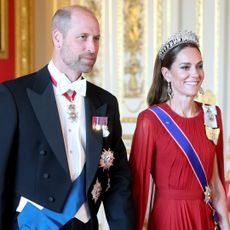 Prince William walking with Princess kate wearing a red gown and tiara at French state banquet