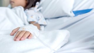 This image shows the mid-section of a young girl in a hospital bed with an IV in her hand.