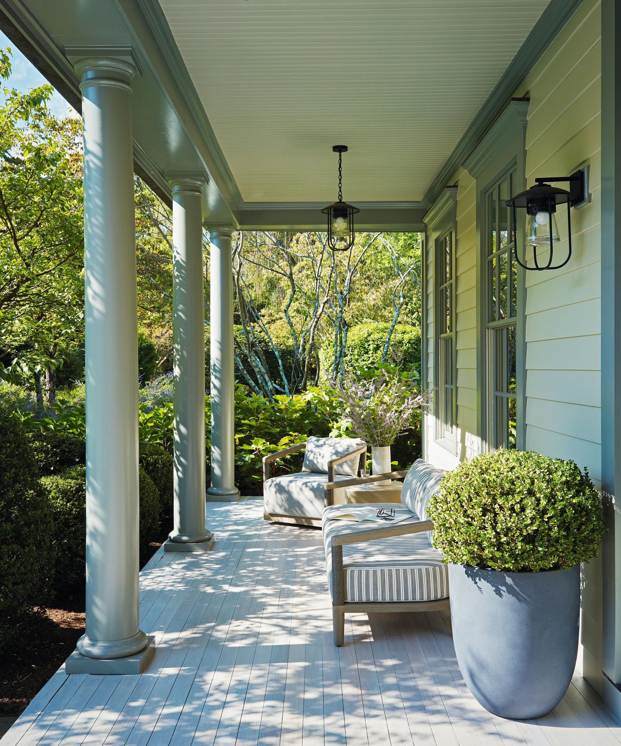 a calm veranda with pillars and a porch area set up with striped sofas and potted plants