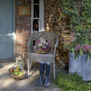 Wicker chair with basket of flowers on next to fruit basket and wellington boots