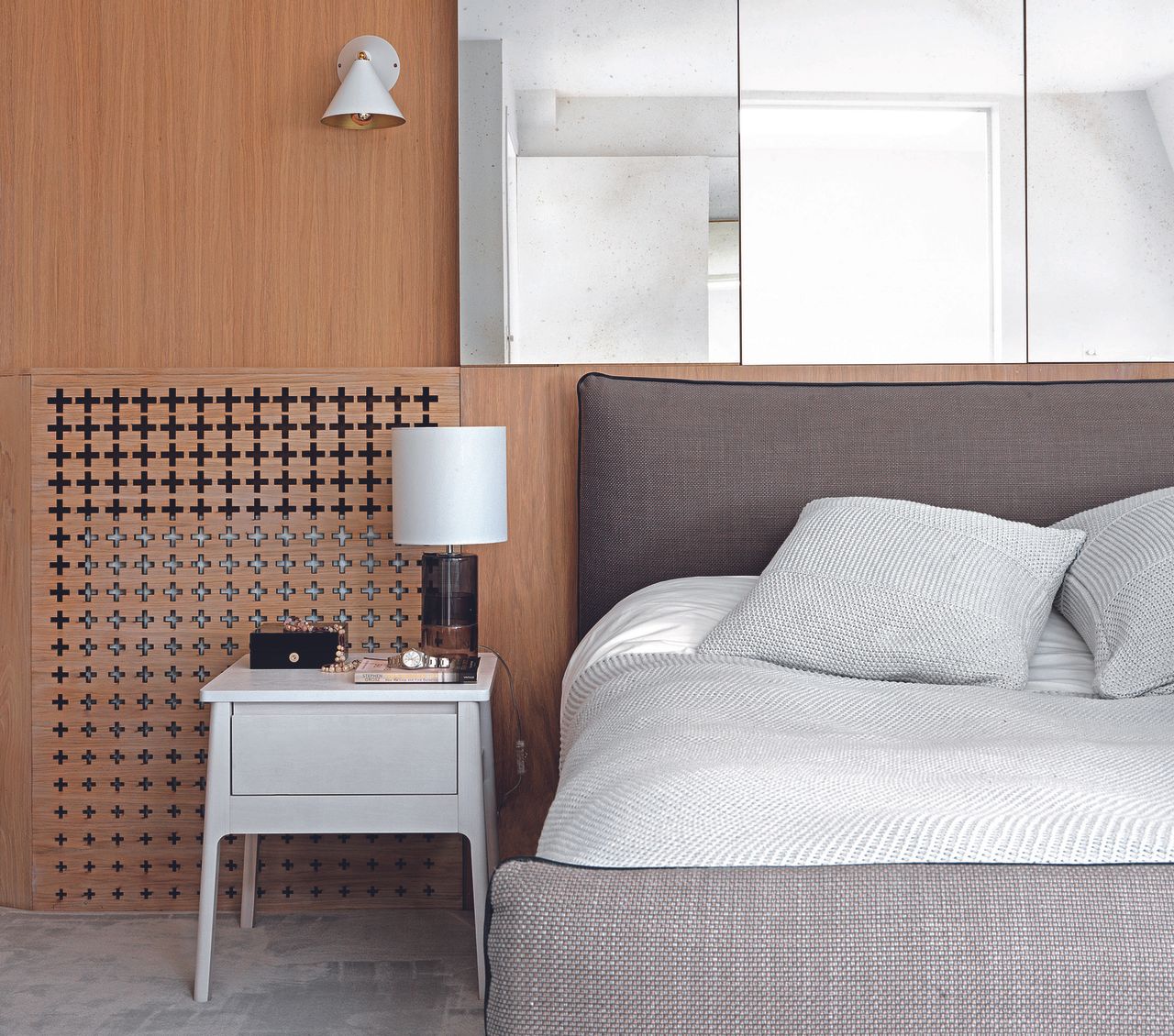 A neutral bedroom with grey bed and headboard, and mirrored glass panel