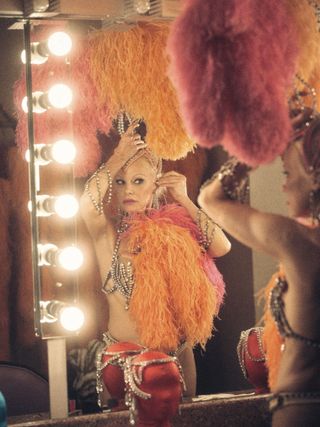 pamela anderson wears feathers and a vegas showgirl outfit and gets ready in a dressing room mirror in a still from the last showgirl