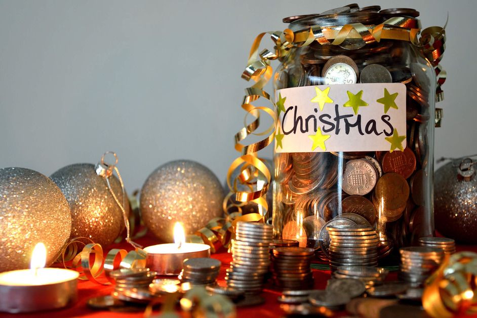 A Christmas savings jar full of coins. Next to it are some tea lights and Christmas baubles. 