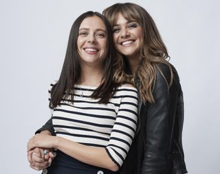 A studio shot of Bel Powley in a white and blue Breton top as Birdy, and Emma Appleton in a black leather jacket as Maggie. Maggie has her arm around Birdy's waist