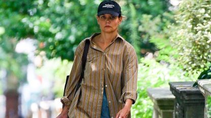 katie holmes wearing a big shirt and short denim shorts with a black bag and baseball cap