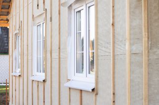 Wall, pediment of a house under construction with windows, vertical beams and a protective membrane, for wall cladding