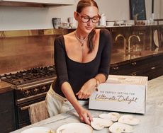 Jenna Lyons standing in a kitchen touch a set of plates laid out on the island 