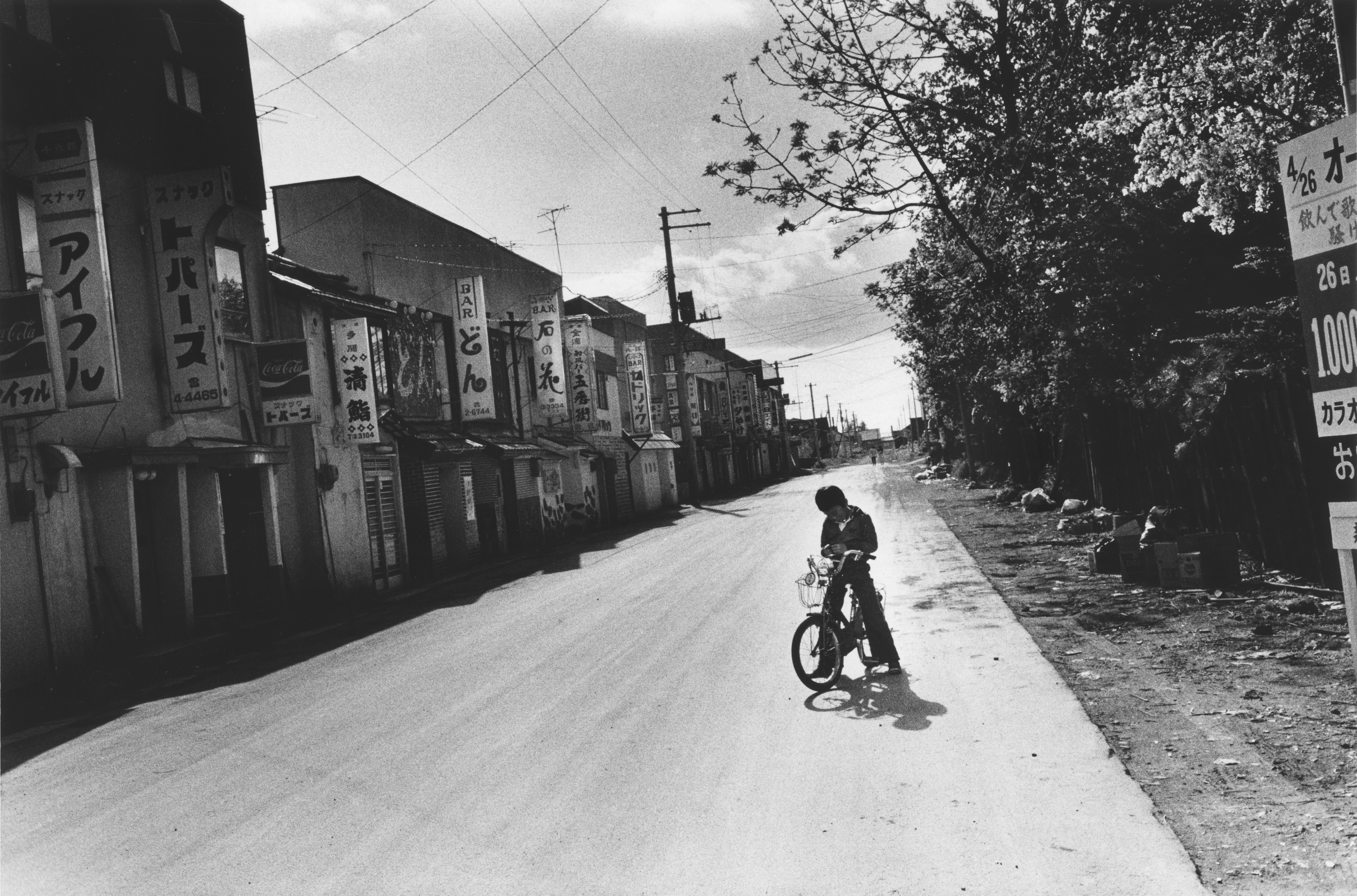 Black and white photograph of a young per-son riding a bicycle on a street.